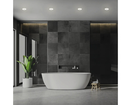 Modernes Badezimmer mit freistehender Badewanne vor einer Wand aus dunklen quadratischen Fliesen und integriertem Wandregal.
