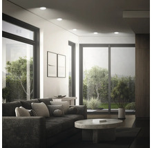 Modernes Wohnzimmer mit Einbaustrahlern an der Decke, Sofa, Couchtisch und großen Fensterfronten mit Blick in den Garten.