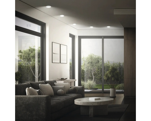 Modernes Wohnzimmer mit Einbaustrahlern an der Decke, Sofa, Couchtisch und großen Fensterfronten mit Blick in den Garten.