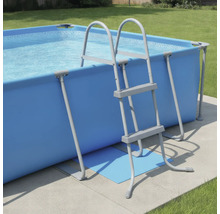 Rechteckiger Aufstellpool in Blau mit grauer Poolleiter in einem hellen Garten auf einer Betonfläche.