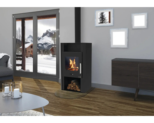 Schwarzer Kaminofen mit Sichtscheibe und brennendem Feuer in modernem Wohnzimmer mit Holzboden und Ausblick auf verschneite Berge.