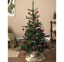 Künstlicher Tannenbaum dekoriert mit roten Christbaumkugeln in einem hellen Wohnzimmer auf Holzboden.