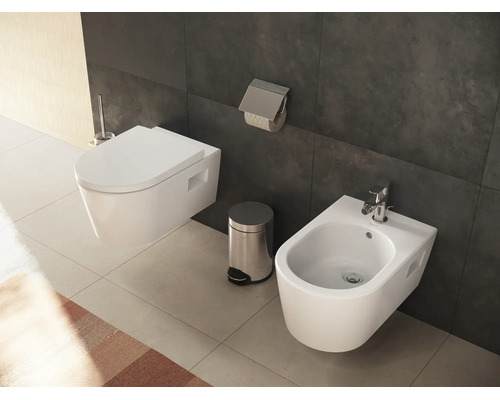 Modernes Badezimmer mit wandhängendem WC, Bidet mit verchromter Armatur, Treteimer und Toilettenpapierhalter vor dunklen Fliesen.