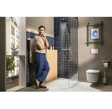 Modernes Badezimmer mit ebenerdiger Dusche, dunkelblauen und beigen Wandfliesen sowie einem Wand-WC. Ein Mann steht im hellen, organisierten Raum.