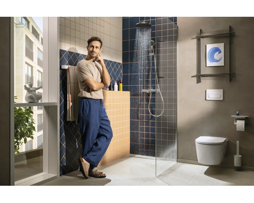 Modernes Badezimmer mit ebenerdiger Dusche, dunkelblauen und beigen Wandfliesen sowie einem Wand-WC. Ein Mann steht im hellen, organisierten Raum.