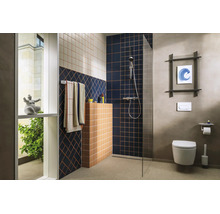 Modernes Badezimmer mit bodengleicher Dusche, Glaswand, geometrischen Fliesenmustern, wandhängender Toilette und verchromten Armaturen.