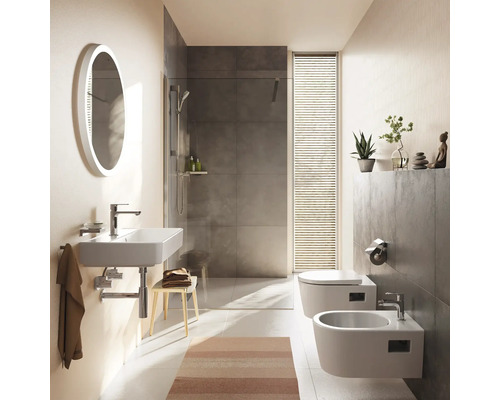 Modernes Badezimmer mit wandhängendem Waschbecken, ovalem Spiegel, begehbarer Dusche mit grauen Fliesen, Wand-Toilette und Bidet. Hell strukturiert.