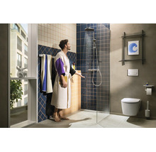 Modernes Badezimmer mit begehbarer Dusche, Regenduschkopf, Wand-WC und blau-beigen Fliesen. Ein Mann im Bademantel prüft das Duschwasser.