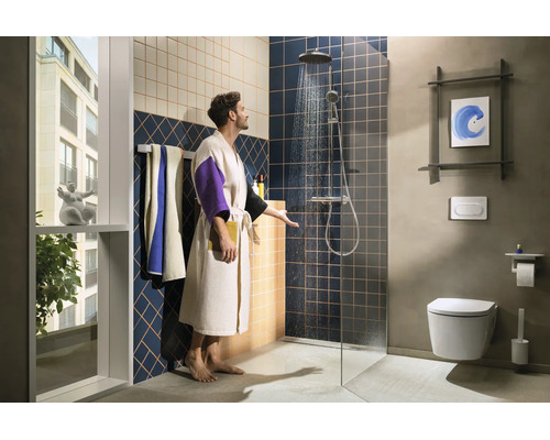 Modernes Badezimmer mit begehbarer Dusche, Regenduschkopf, Wand-WC und blau-beigen Fliesen. Ein Mann im Bademantel prüft das Duschwasser.