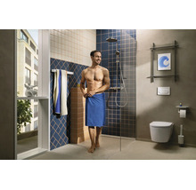 Modernes Badezimmer mit begehbarer Dusche, Glaswand, wandhängender Toilette, gemusterten Wandfliesen und einem Mann mit Handtuch.