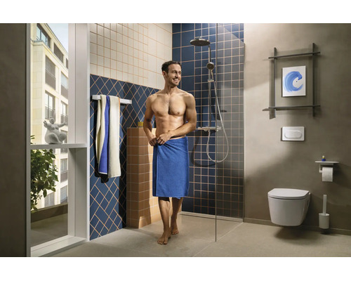 Modernes Badezimmer mit begehbarer Dusche, Glaswand, wandhängender Toilette, gemusterten Wandfliesen und einem Mann mit Handtuch.