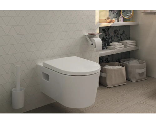 Modernes, wandhängendes WC mit Deckel, Toilettenbürste und Papierhalter mit Ablage in einem hellen Badezimmer mit Fliesen in Dreiecksoptik.