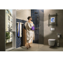 Modernes Badezimmer mit Person im Bademantel, bodengleicher Dusche, Glastrennwand, Regenduschkopf, Wand-WC, Handtuchhalter und großem Fenster.