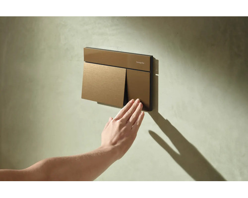 Hansgrohe Betätigungsplatte für Toilettenspülung an einer strukturierten Wand, eine Hand betätigt die kleine Spültaste.