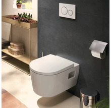 Modernes Wand-WC im Badezimmer mit Drückerplatte, Toilettenpapierhalter und Abfalleimer vor dunklen Wandfliesen.