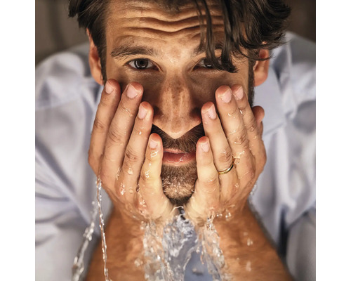 Nahaufnahme eines Mannes mit Bart, der sich das Gesicht mit klarem Wasser wäscht.