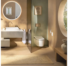 Modernes Badezimmer mit weißem Aufsatzwaschbecken, rundem Leuchtspiegel, Wand-WC und Naturteppich in erdigen Tönen.
