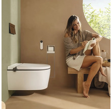 Modernes Badezimmer mit wandhängendem Dusch-WC, Fernbedienung und Drückerplatte. Eine Frau sitzt auf einer Holzbank in hellem Ambiente.