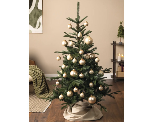 Dekorierter Weihnachtsbaum mit goldenen Kugeln und einer beigen Baumdecke in einem gemütlichen Wohnzimmer.