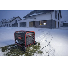 Einhell Stromerzeuger im winterlichen Außeneinsatz vor einem Wohnhaus im Schnee, liefert Strom über ein Kabel.