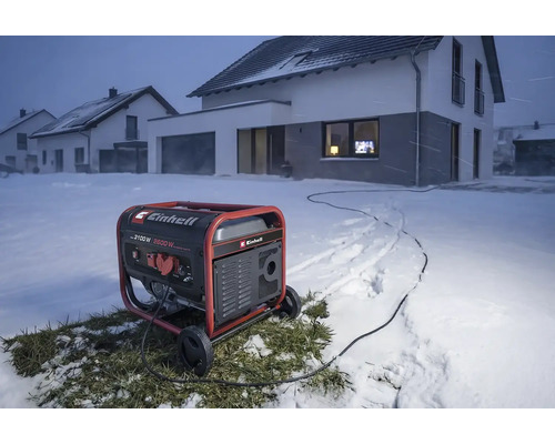 Einhell Stromerzeuger im winterlichen Außeneinsatz vor einem Wohnhaus im Schnee, liefert Strom über ein Kabel.