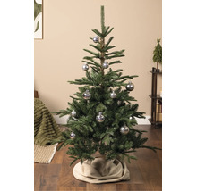 Künstlicher Weihnachtsbaum mit silbernen Christbaumkugeln mit Schneeflockenmotiv auf Holzboden in einem hellen Wohnraum.