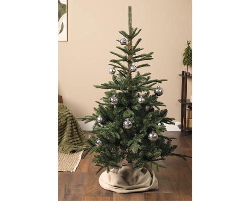 Künstlicher Weihnachtsbaum mit silbernen Christbaumkugeln mit Schneeflockenmotiv auf Holzboden in einem hellen Wohnraum.