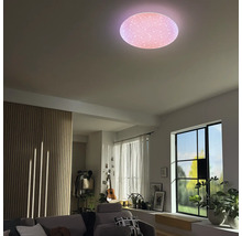 Runde LED-Deckenleuchte mit Sterneneffekt in einem hellen Wohnzimmer mit Holzlamellenwand, Sofa und großen Fenstern.