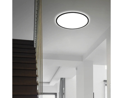 Moderne runde LED-Deckenleuchte in einem hellen Raum mit einer dunklen Holztreppe.