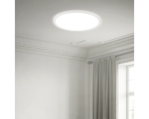 Runde LED-Deckenleuchte in einem hellen, klassisch gestalteten Raum mit Stuckverzierungen und Vorhängen.