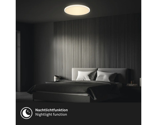 Runde LED-Deckenleuchte mit Nachtlichtfunktion in einem modern eingerichteten Schlafzimmer mit Wandpaneelen aus Holz.