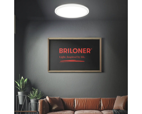 Moderne Wohnzimmerszene mit einer hellen, runden LED-Deckenleuchte, einem Ledersofa und Zimmerpflanzen vor einer dunklen Wand. Briloner Logo.