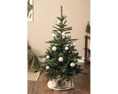 Hell dekorierter künstlicher Weihnachtsbaum in einem Wohnzimmer, geschmückt mit weißen Christbaumkugeln mit Karomuster und einer beigen Baumdecke.
