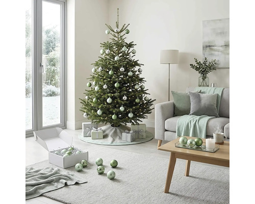 Festlich geschmückter Weihnachtsbaum in einem hellen Wohnzimmer mit Sofa, Couchtisch aus Holz sowie silbernen und grünen Christbaumkugeln.