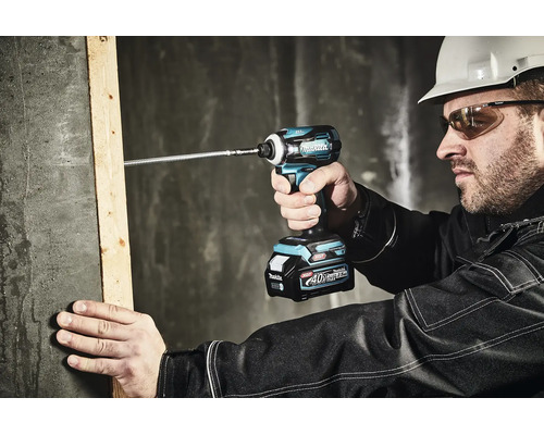 Bauarbeiter schraubt mit einem Makita 40 Volt Akku-Schlagschrauber eine lange Schraube in einen Holzbalken an einer Betonwand.