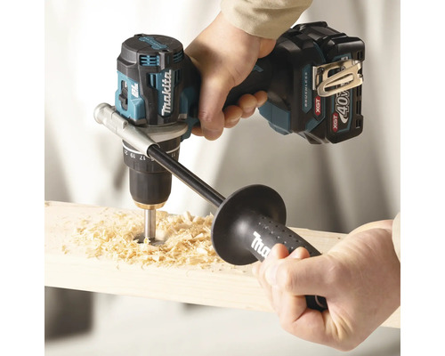 Makita Akku-Bohrschrauber 40 Volt bohrt mit Zusatzhandgriff ein Loch in ein Holzbrett, wobei Holzspäne entstehen.