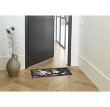 Fußmatte mit floralem Muster in einem hellen Flur mit Holzboden neben einer Tür und einer Bodenvase.