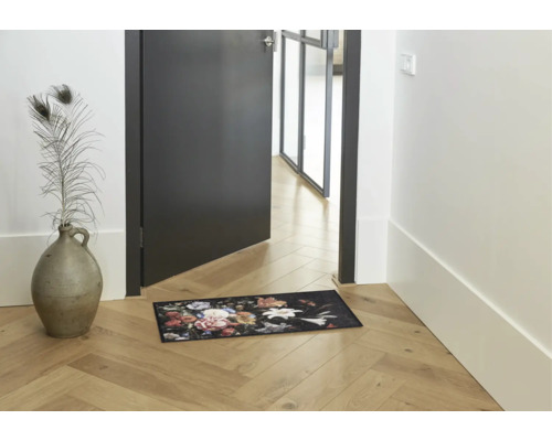 Fußmatte mit floralem Muster in einem hellen Flur mit Holzboden neben einer Tür und einer Bodenvase.