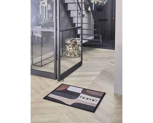 Moderne Diele mit einer Fußmatte mit geometrischem Muster und dem Schriftzug home auf Fischgrätboden neben einer Glastür.
