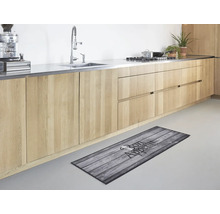 Moderne Küche mit hellen Holzelementen und einem Küchenläufer in Holzoptik mit der Aufschrift Bon Appetit auf dem hellen Fußboden.