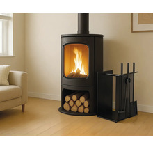 Moderner schwarzer Kaminofen mit brennendem Feuer und Holzfach in einem hellen Wohnzimmer mit Sofa und Kaminbesteck.