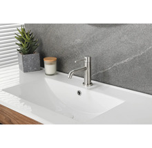 Modernes weißes Keramik-Waschbecken mit einer Einhand-Waschtischarmatur aus gebürstetem Metall, einer Sukkulente und Kerze vor einer Steinwand.