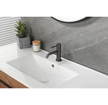 Modernes Badezimmer mit weißem Waschtisch, schwarzer Waschtischarmatur, grauer Wand in Steinoptik und hölzernem Unterschrank.
