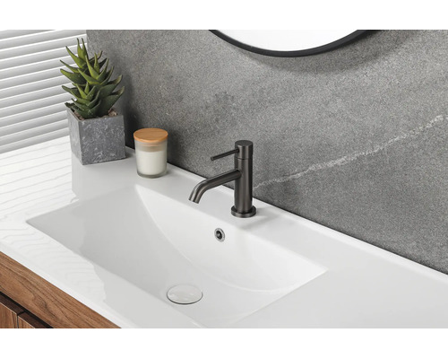 Modernes Badezimmer mit weißem Waschtisch, schwarzer Waschtischarmatur, grauer Wand in Steinoptik und hölzernem Unterschrank.