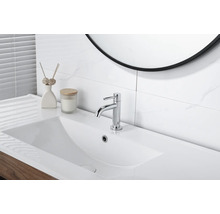 Moderne Waschtischarmatur in Chrom auf einem weißen Waschbecken in einem hellen Badezimmer mit Fliesen in Marmoroptik.