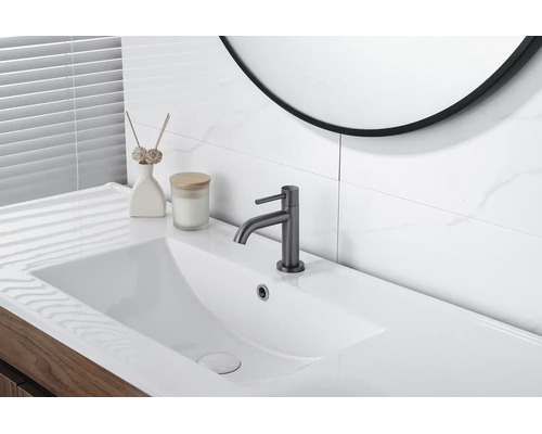 Helles, modernes Badezimmer mit weißem rechteckigem Waschbecken, dunkelgrauer Armatur, Holz-Waschtischunterschrank und weißen Fliesen in Marmoroptik.