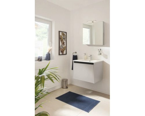 Modernes Badezimmer mit weißem Hängewaschbeckenunterschrank, Spiegelschrank, Armatur und blauem Badteppich in hellem Ambiente.