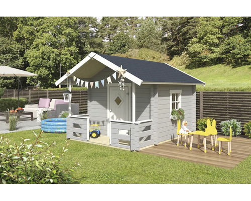 Ein graues Kinderspielhaus aus Holz mit Satteldach, kleiner Veranda und weißen Akzenten in einem hellen Garten mit Spielzeug und Loungemöbeln.