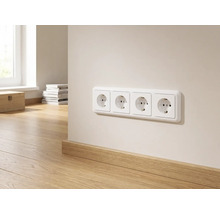 Vierfache Steckdose an einer hellen Wand über einer Holzsockelleiste in einem hellen, modern eingerichteten Raum.