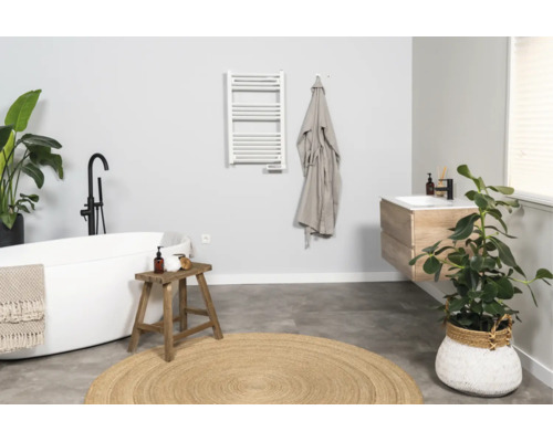 Modernes, helles Badezimmer mit freistehender Badewanne, hölzernem Waschtisch, weißem Handtuchheizkörper und rundem Jute-Teppich.